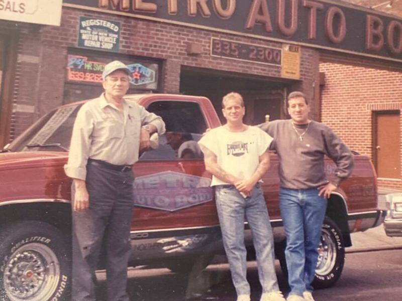 Three men posing with a Metro Auto Body pickup in front of the shop's original storefront