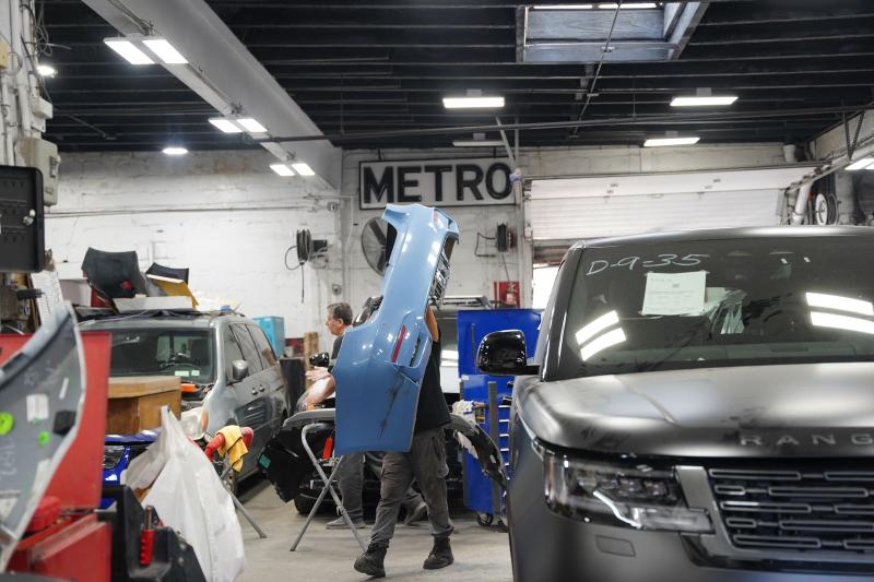 Metro Auto Body technician carrying a repaired bumper under the shop's METRO sign