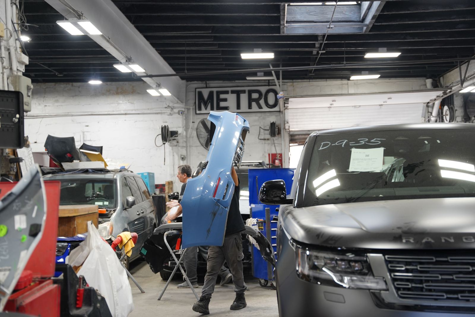 Metro Auto Body technician carrying a genuine replacement bumper on the shop floor